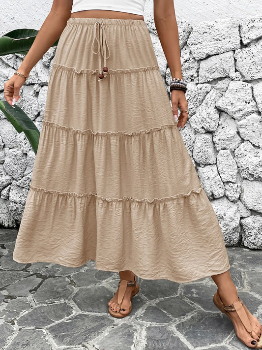 Person wearing a beige tiered skirt against a stone wall.