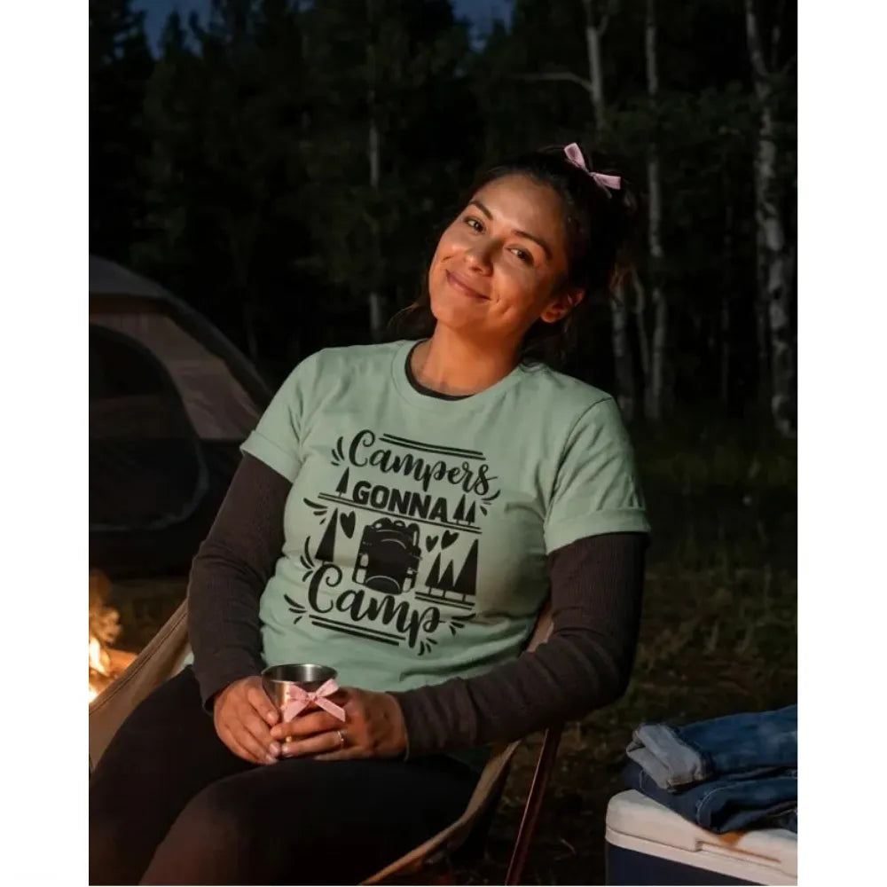 Woman in green campers gonna camp t-shirt with long sleeve undershirt. sitting in a camp chair with a wooded background