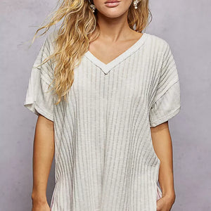 Woman wearing a light gray ribbed t-shirt against a plain background