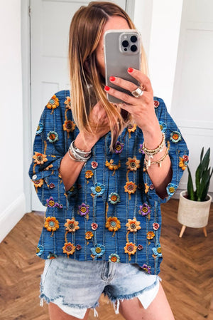 Woman taking a mirror selfie wearing a blue floral top and denim shorts.