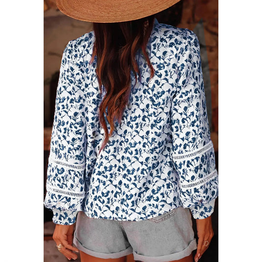 Person wearing a blue floral blouse with long sleeves and gray shorts, partially obscured by a straw hat.