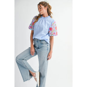 Woman wearing a light blue blouse with floral sleeves and high-waisted jeans on a white background