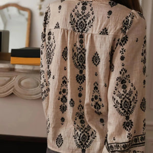 Beige blouse with black floral patterns worn by a person, with a blurred indoor background.