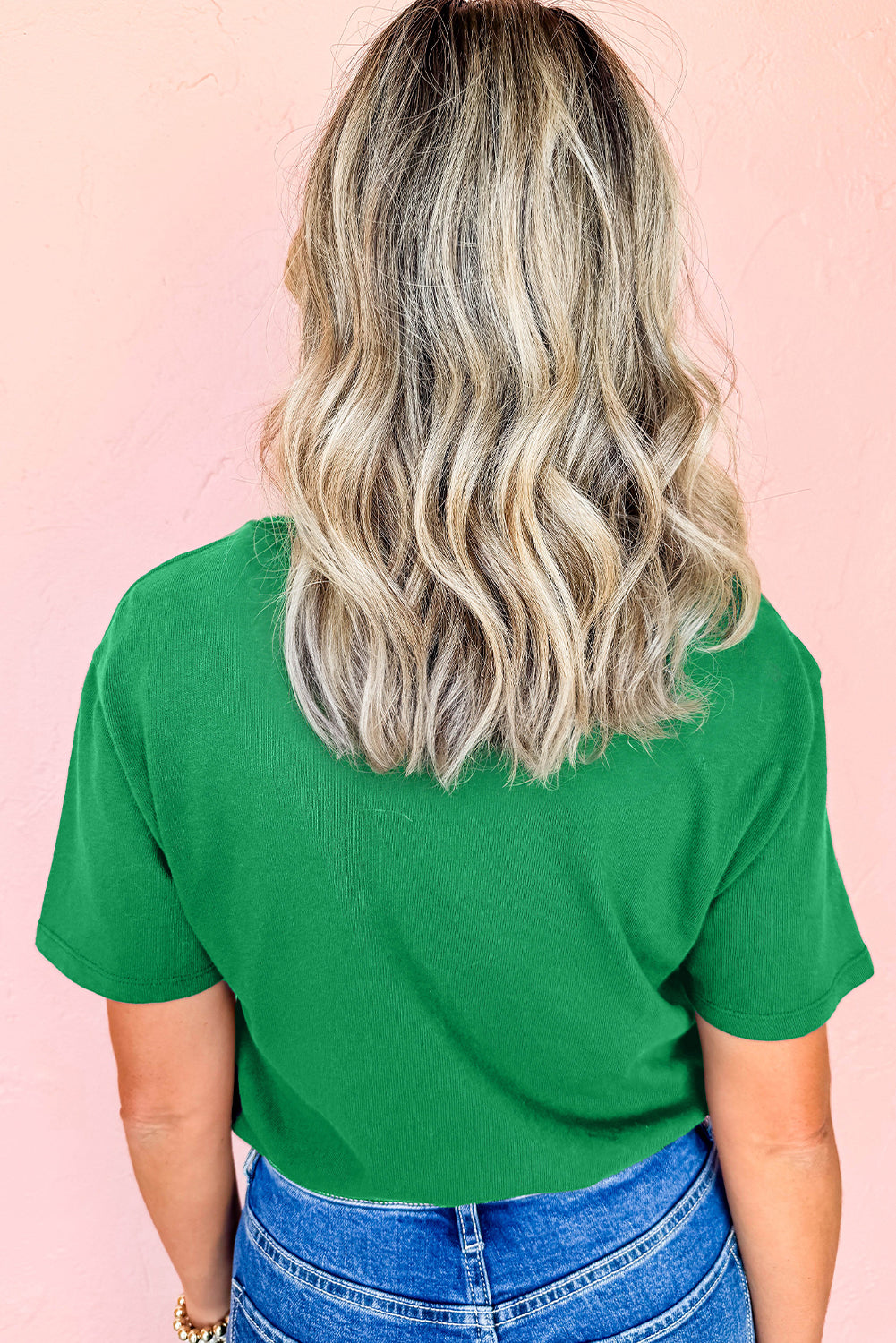 Person wearing a green t-shirt and blue jeans with a pink background