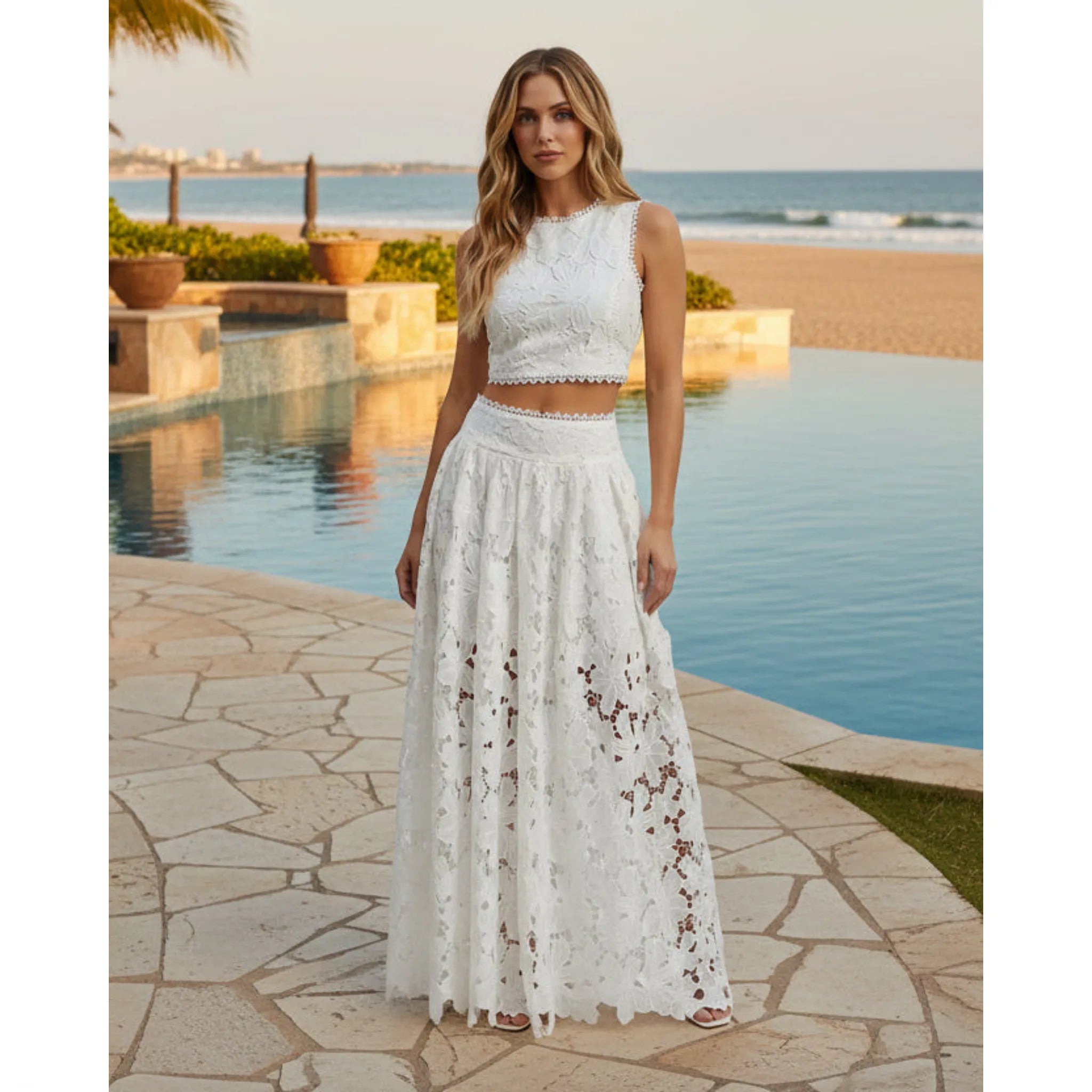 Woman in a white lace dress standing by a pool with ocean view