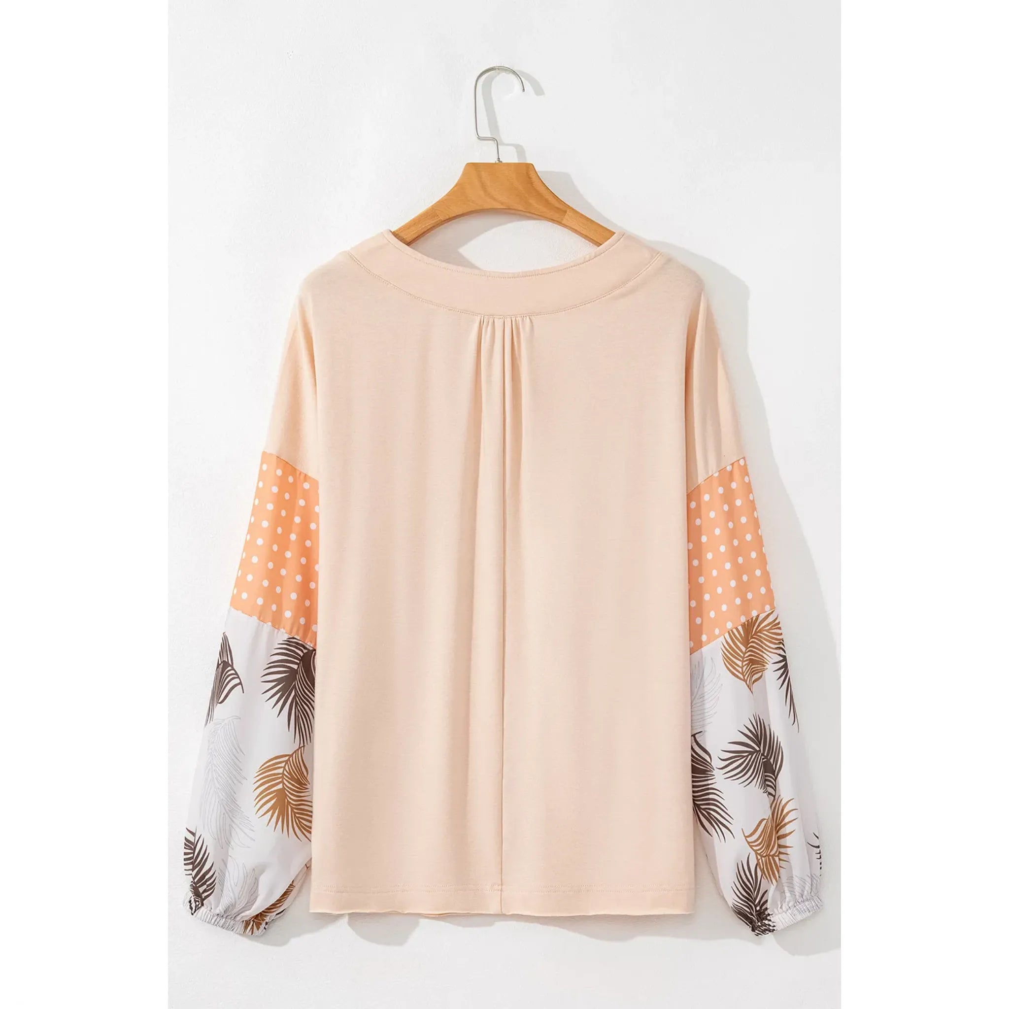 Blouse with polka dot and leaf pattern sleeves on a hanger against a white background