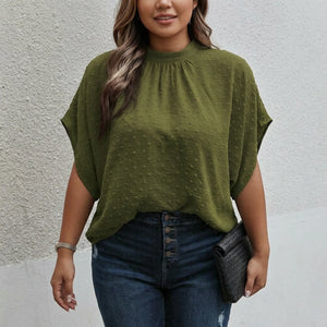 Woman wearing a green top and blue jeans against a gray wall