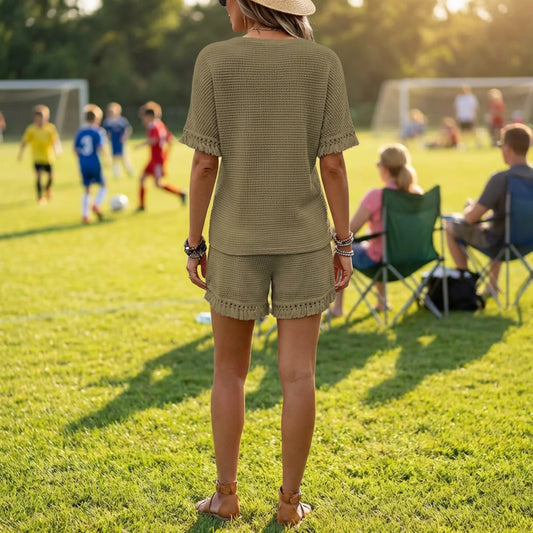 Woman in a green outfit standing on a soccer field with children playing in the background