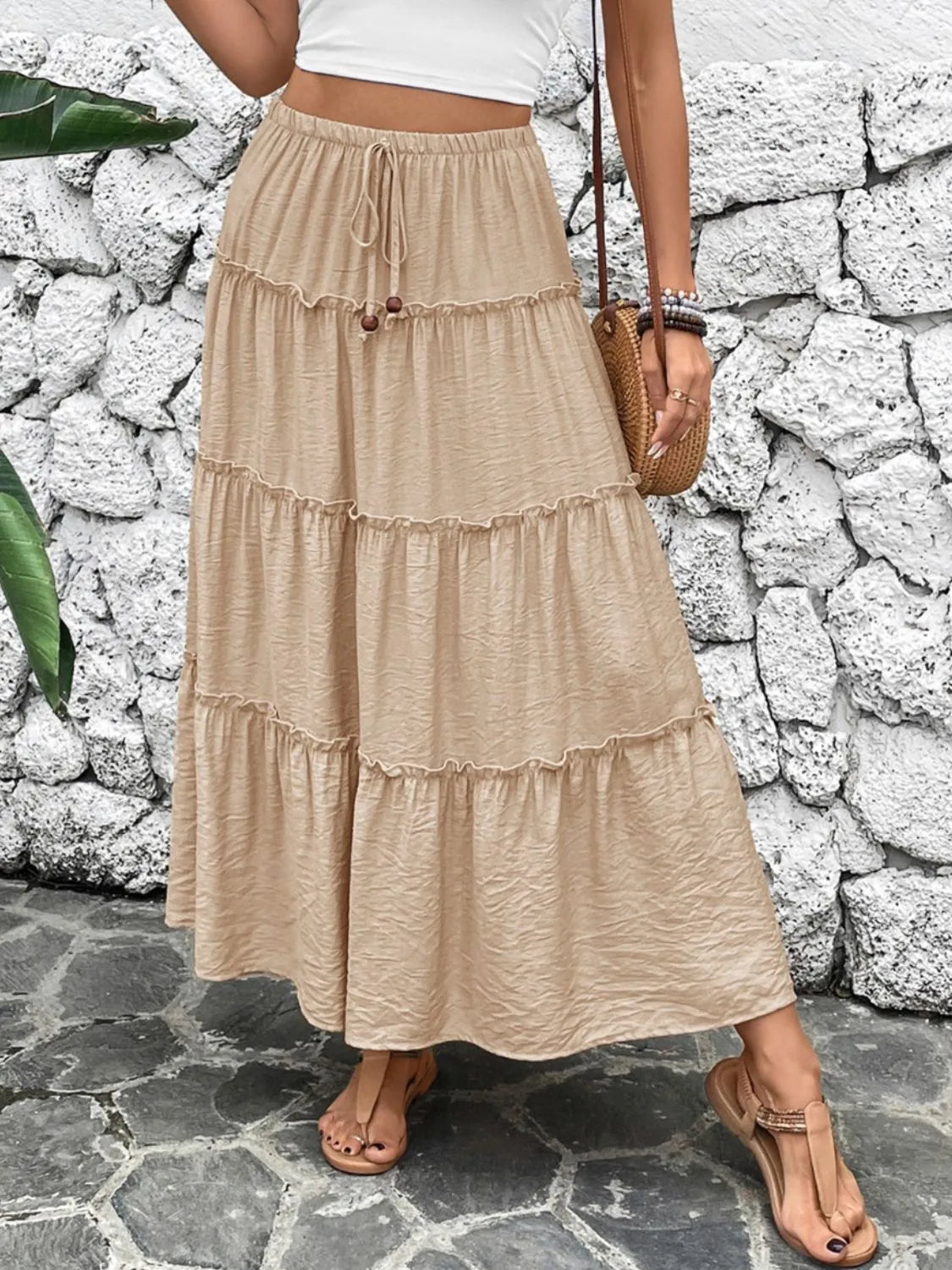 Person wearing a beige tiered skirt against a stone wall.