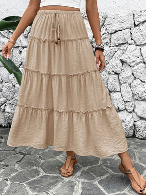 Person wearing a beige tiered skirt against a stone wall.