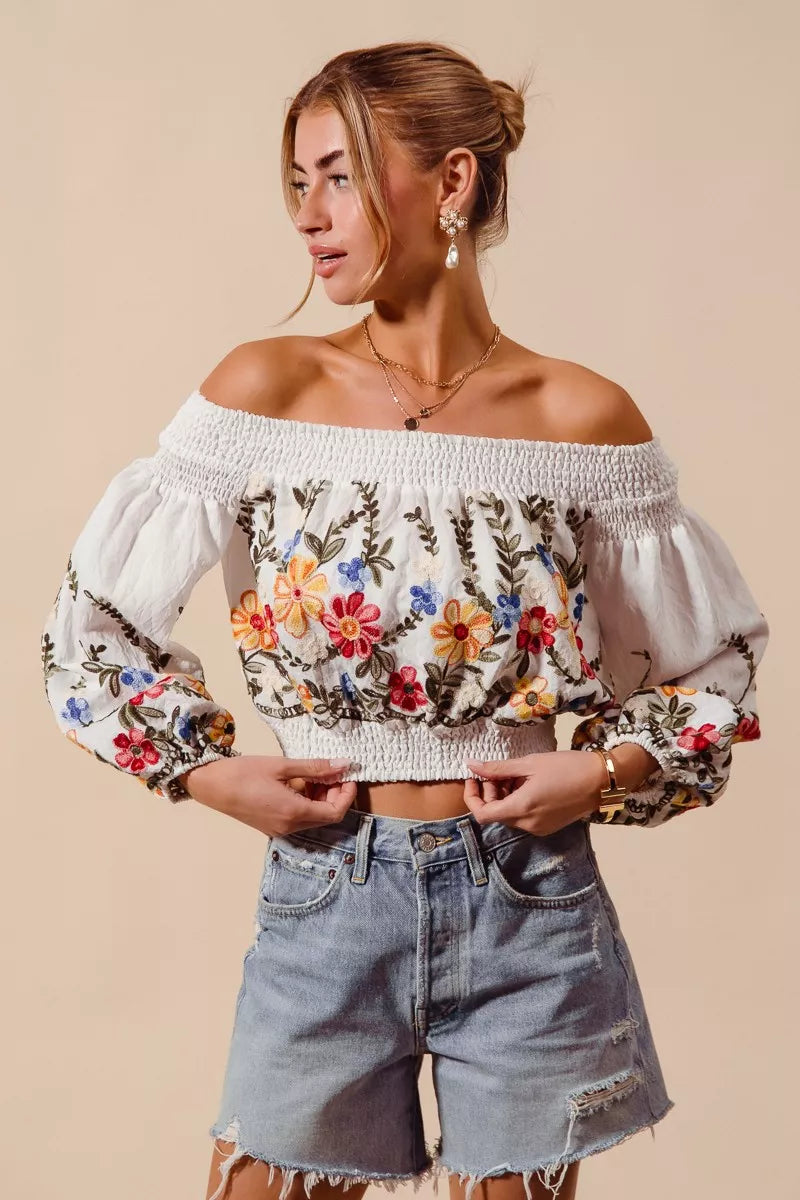Woman wearing a floral off-shoulder top and denim shorts on a beige background