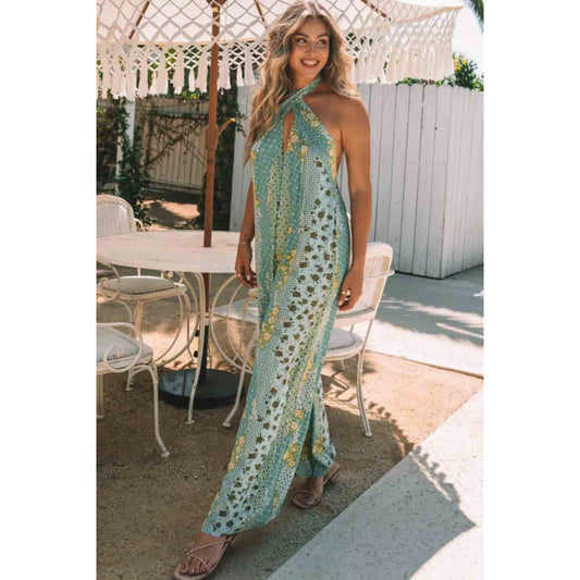 Woman in a green patterned dress standing outdoors near a table and chairs.