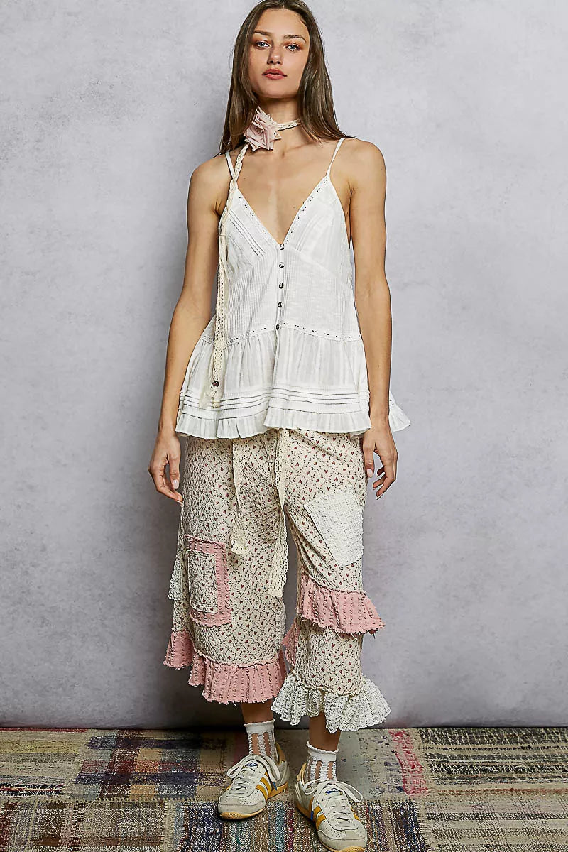 Woman wearing a white lace top and pants with pink accents against a gray background