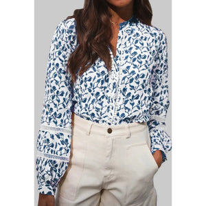 Woman wearing a blue floral blouse and beige pants against a gray background