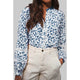 Woman wearing a blue floral blouse and beige pants against a gray background