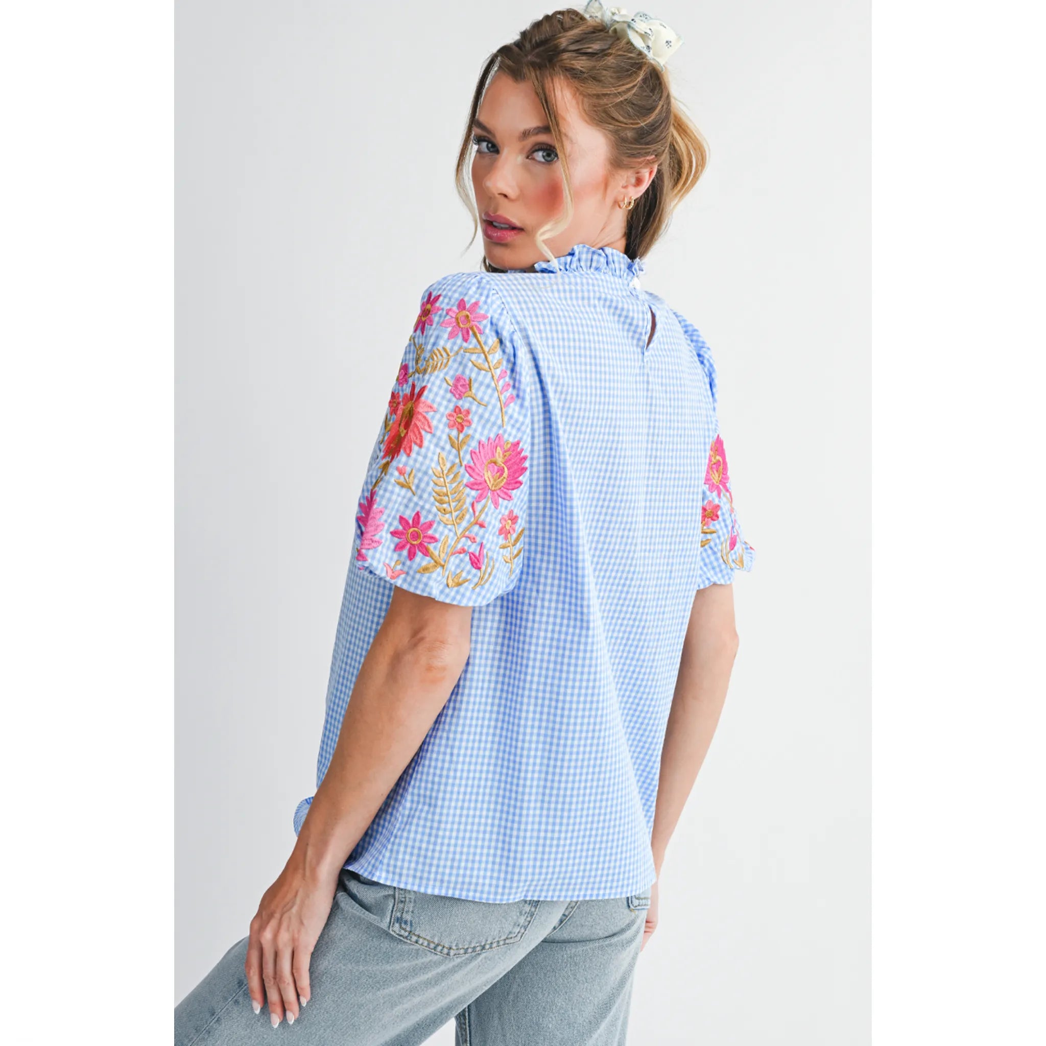 Woman wearing a light blue checkered blouse with floral embroidery on a white background