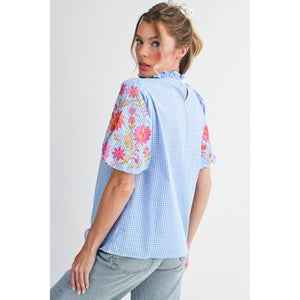 Woman wearing a light blue checkered blouse with floral embroidery on a white background