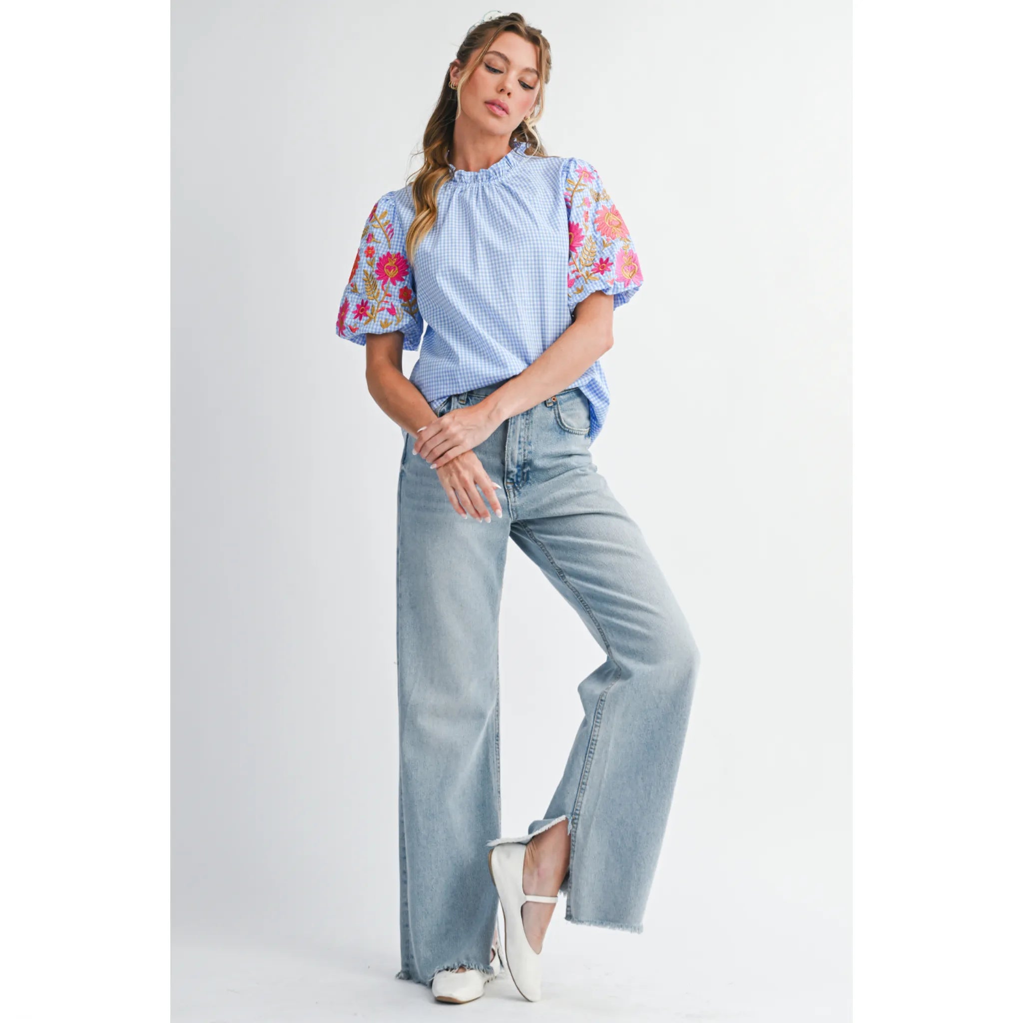 Woman wearing a light blue top with floral sleeves and high-waisted jeans on a white background
