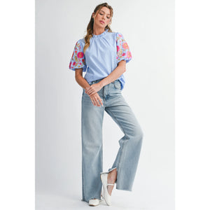 Woman wearing a light blue top with floral sleeves and high-waisted jeans on a white background