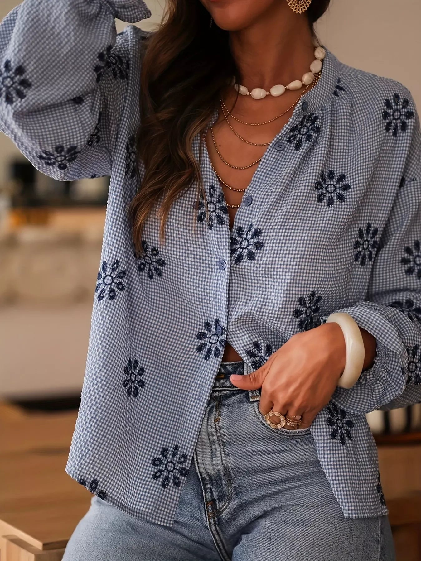 Person wearing a blue floral blouse with rolled-up sleeves and jeans indoors.