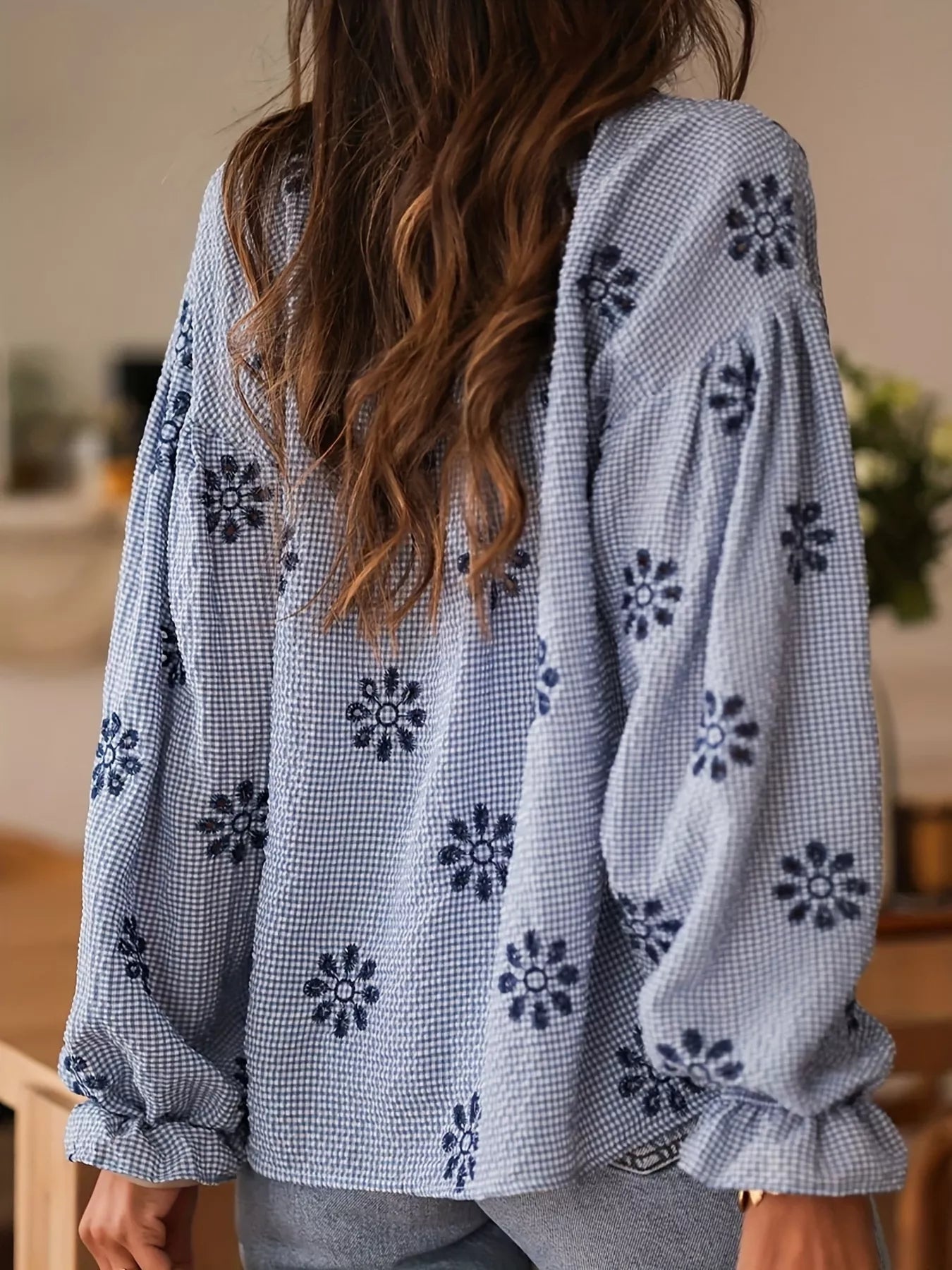 Person wearing a blue floral embroidered blouse with a blurred background