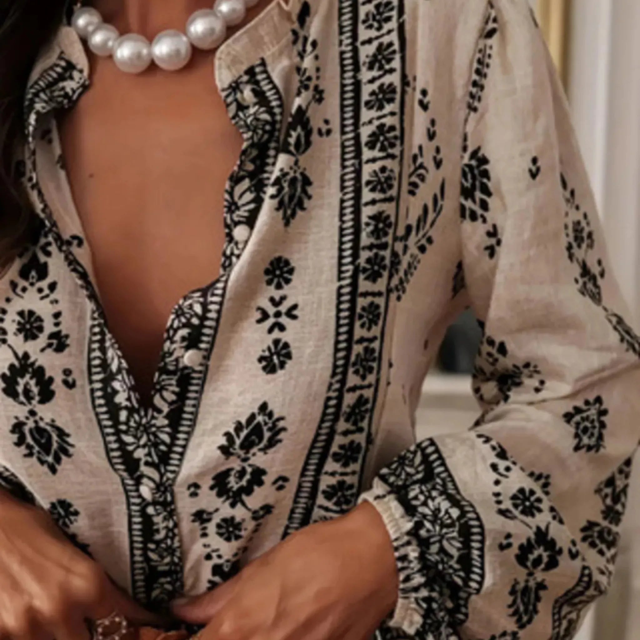 Person wearing a black and white patterned blouse with pearl necklace