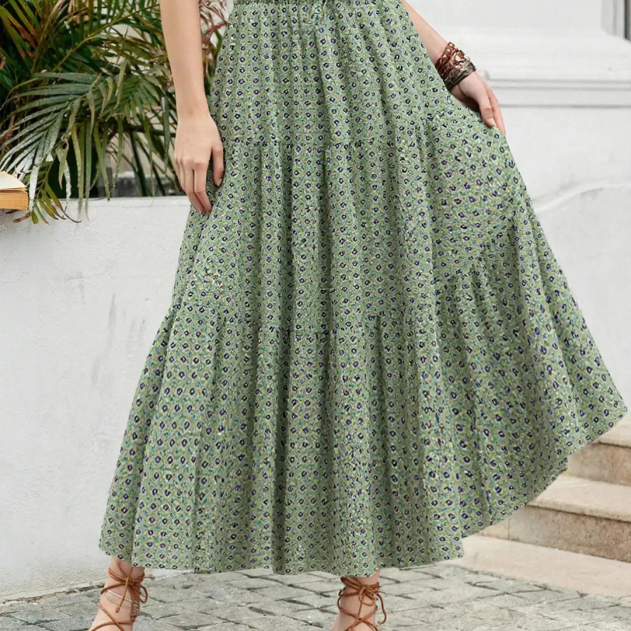 Person wearing a green floral dress standing on steps with a white wall and plant in the background