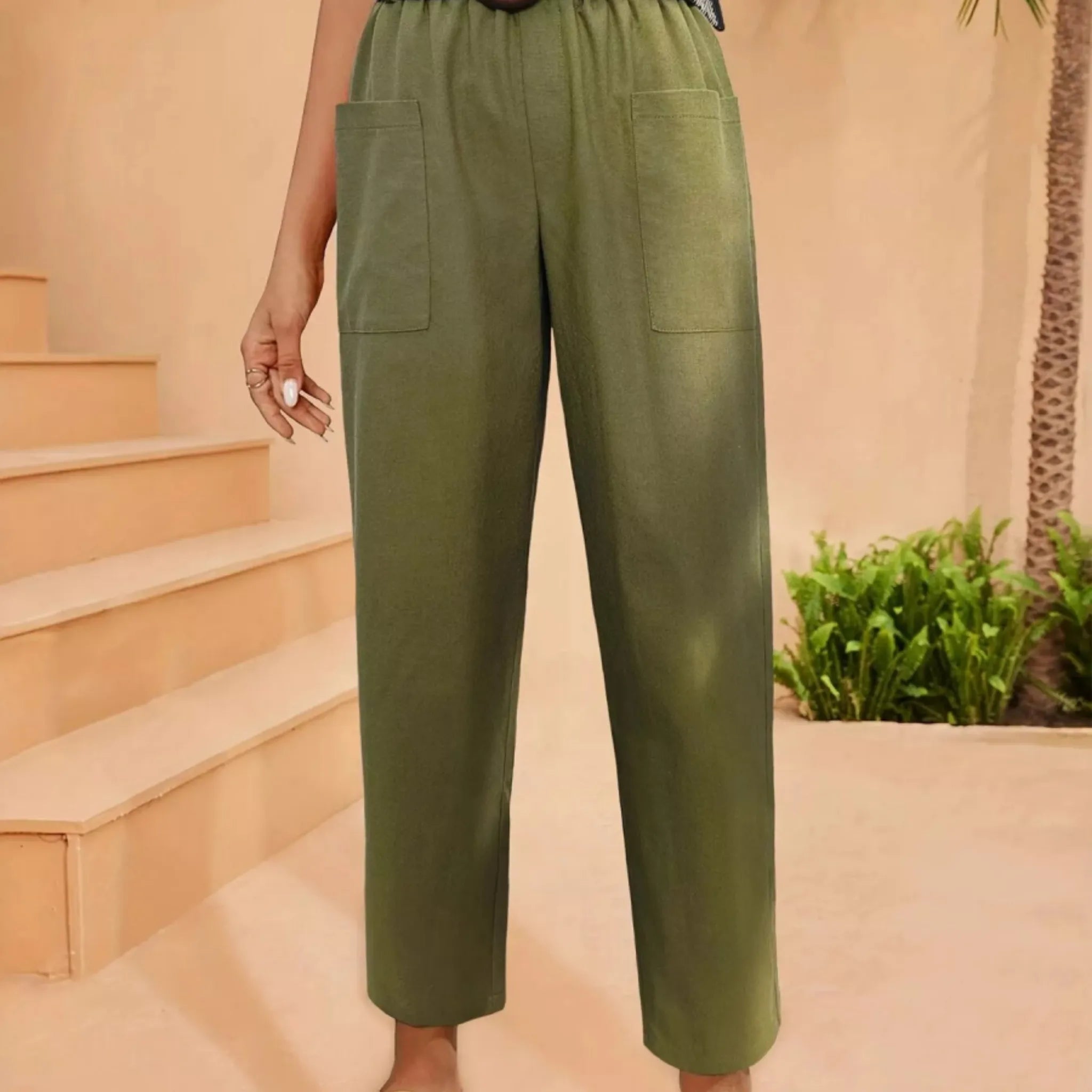 Green pants worn by a person on a peach-colored staircase with plants in the background