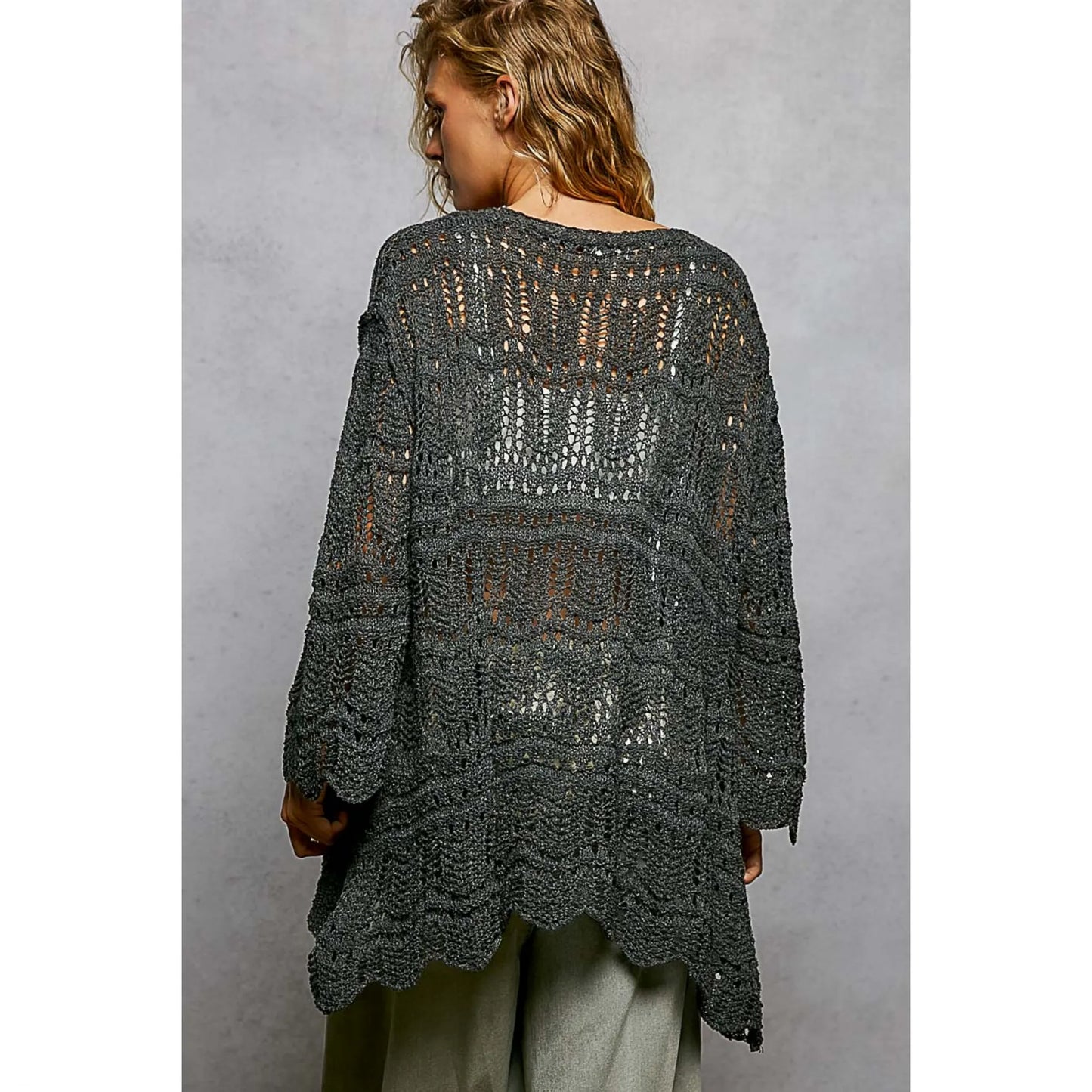 Woman wearing a dark gray crochet cardigan against a plain background