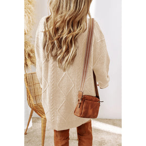 Person wearing a beige cable knit sweater and brown leather bag, standing in a room with a chair and textured wall.