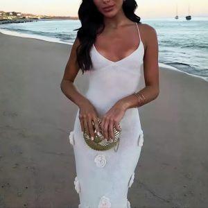 Woman in a white dress on a beach holding a gold clutch.