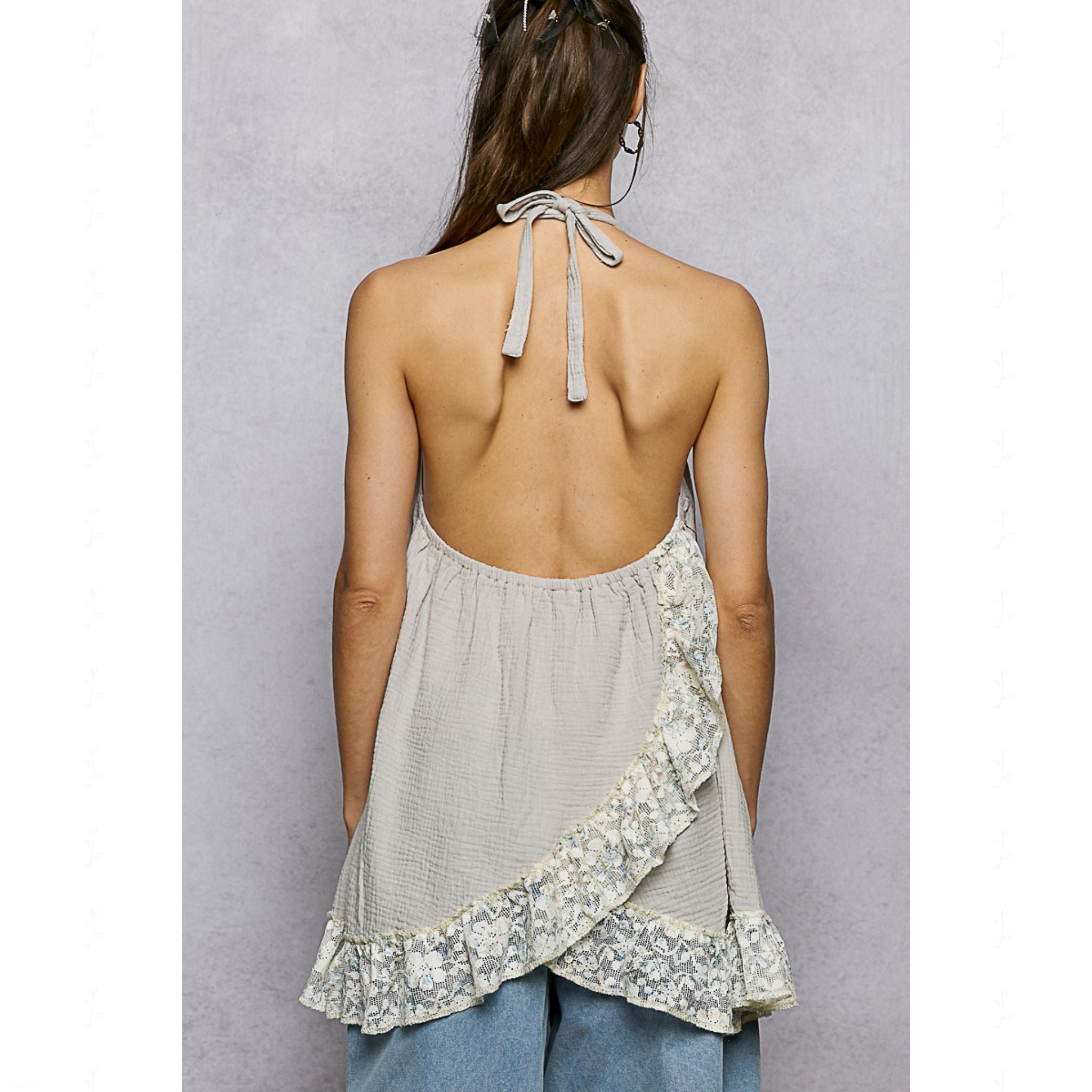 Woman wearing a light gray sleeveless top with floral patterns and tied straps on a plain background