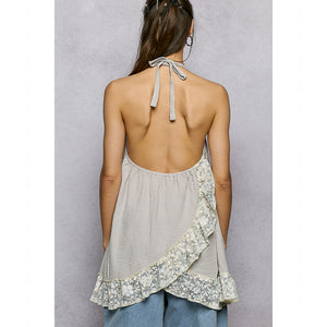 Woman wearing a light gray sleeveless top with floral patterns and tied straps on a plain background