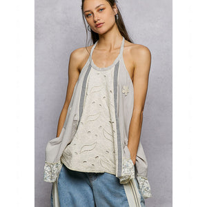 Woman wearing a light-colored sleeveless top with lace details on a gray background