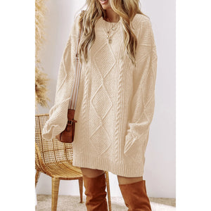 Woman wearing a beige cable knit sweater dress with brown knee-high boots in a minimalistic setting.