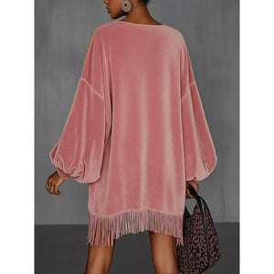 Pink velvet dress with fringe details worn by a person, holding a leopard print bag against a gray background.