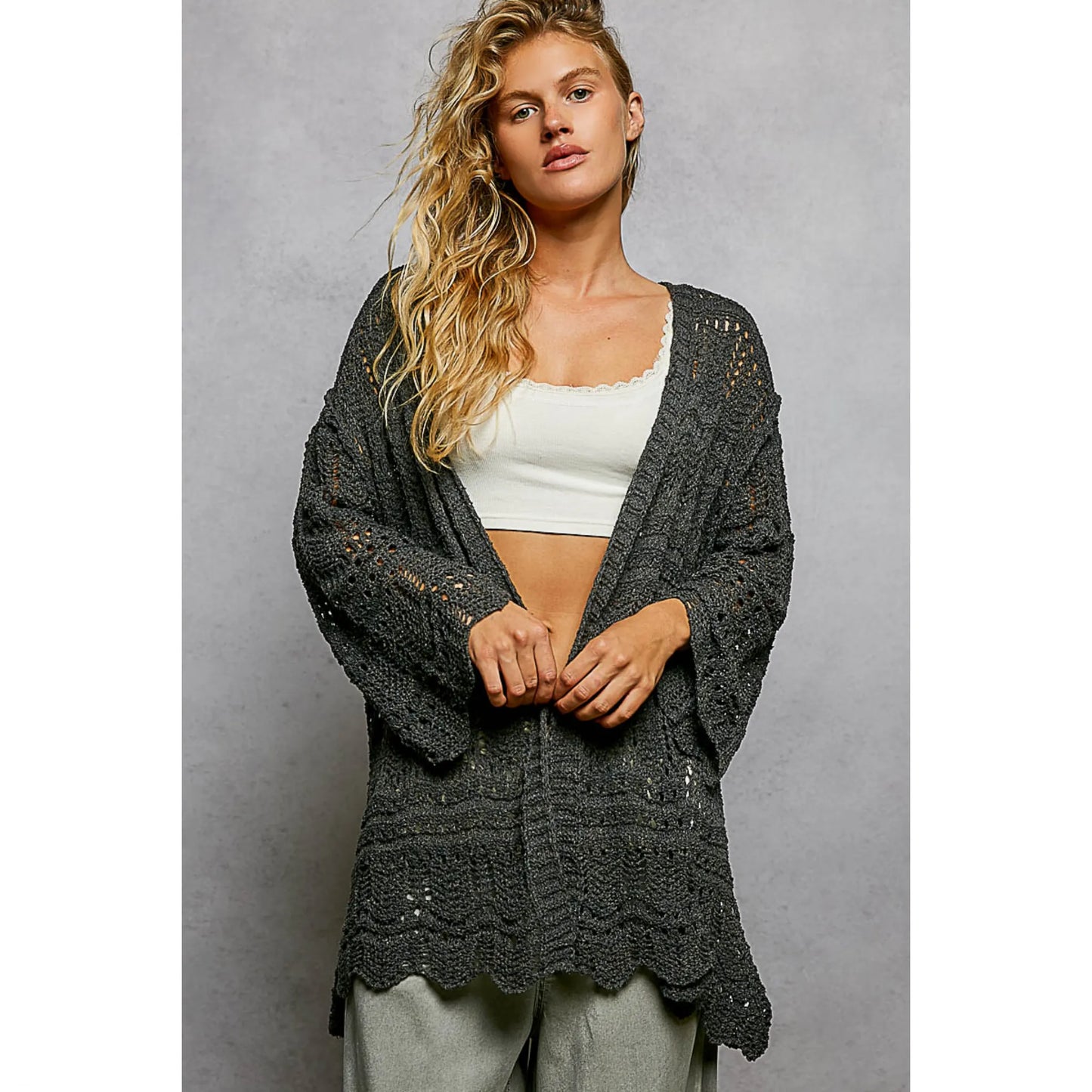 Woman wearing a dark gray crochet cardigan over a white top against a gray background