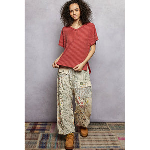 Woman wearing a red top and patterned pants standing against a gray wall.