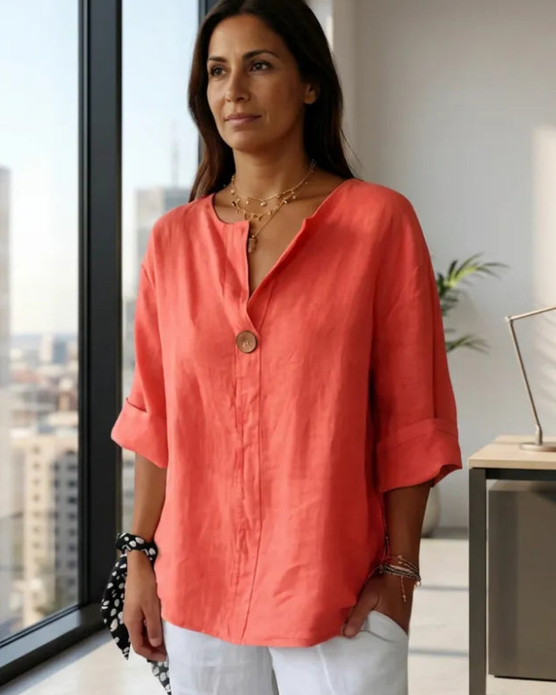 Woman in a coral shirt standing in an office with large windows.