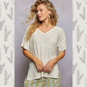 Woman wearing a light-colored ribbed top with a patterned skirt against a gray background with leaf designs.