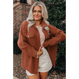 Woman wearing a brown cardigan over a white shirt and shorts, standing outdoors.