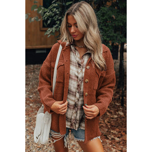 Woman wearing a brown cardigan over a plaid shirt with denim shorts, standing outdoors.
